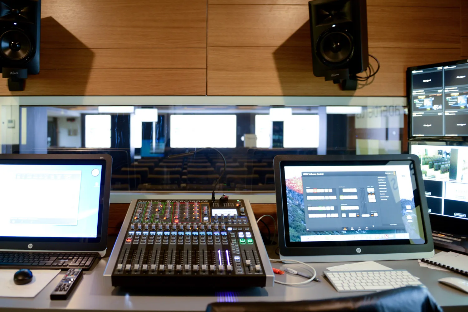 Sala de control con mesa de mezclas, monitores de señal y altavoces de estudio sobre el auditorio.