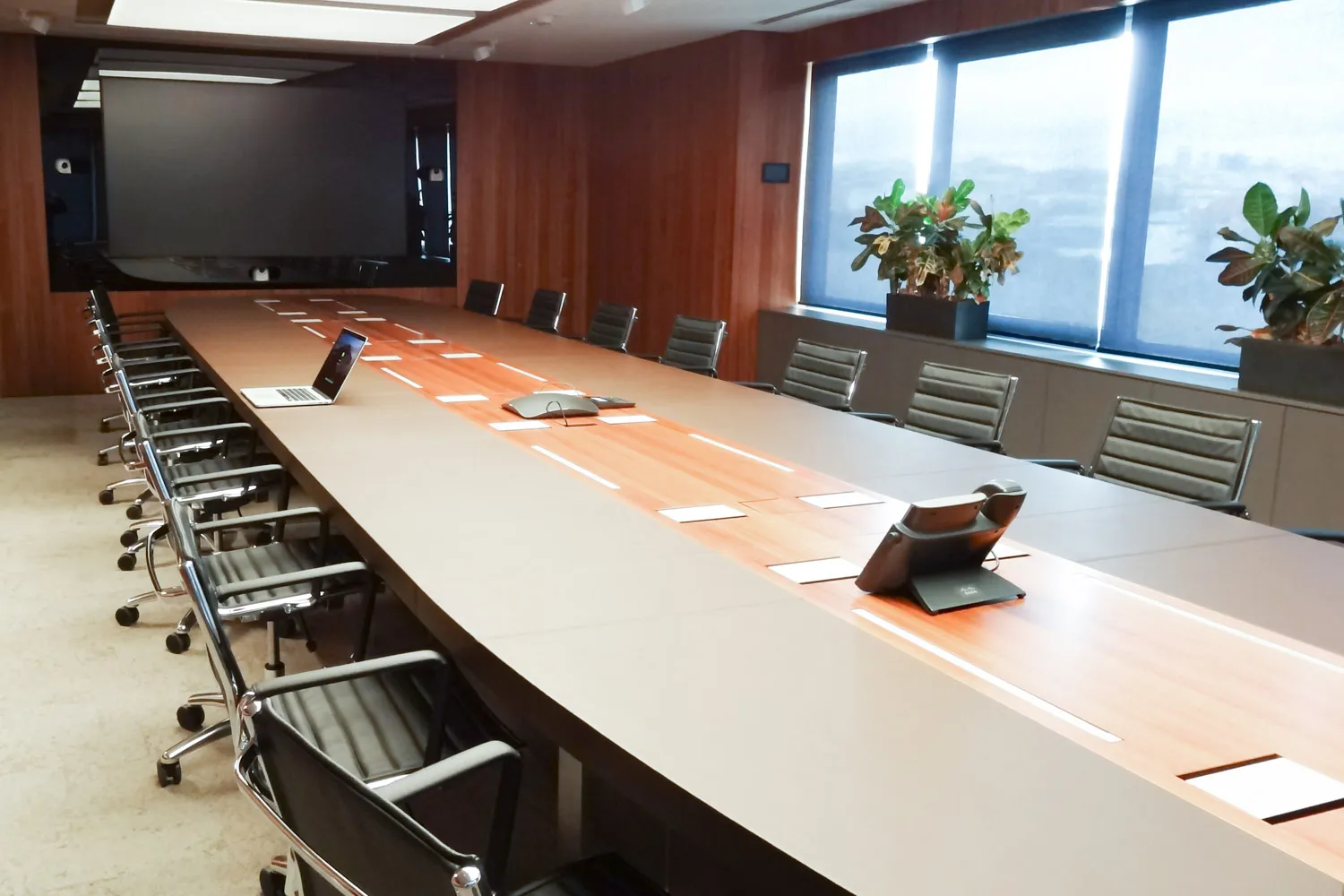 Sala de consejo revestida en madera con mesa de reuniones, pantalla de gran formato y sistema de videoconferencia.