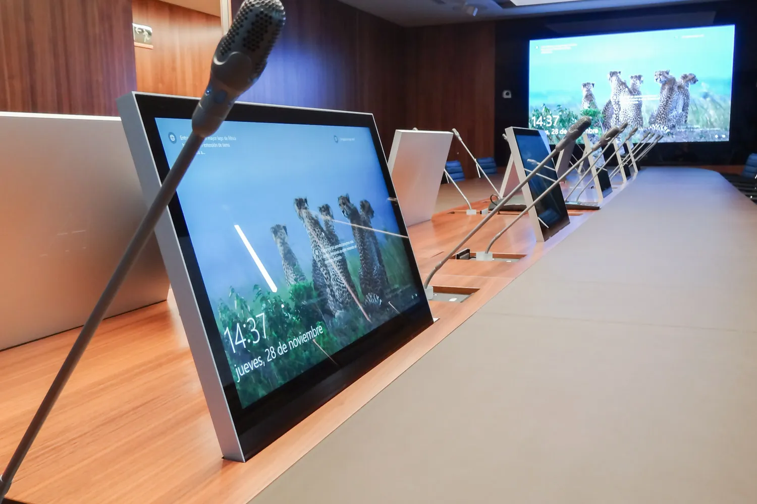Monitores retráctiles y micrófonos de cuello de cisne integrados en una mesa de conferencias.