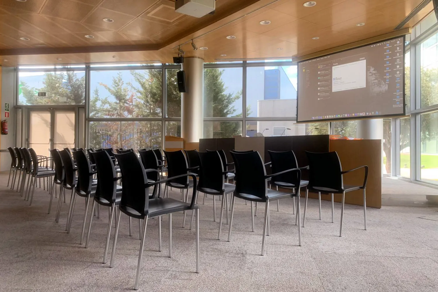 Sala de actos preparada con sillas, atril y pantalla de proyección.