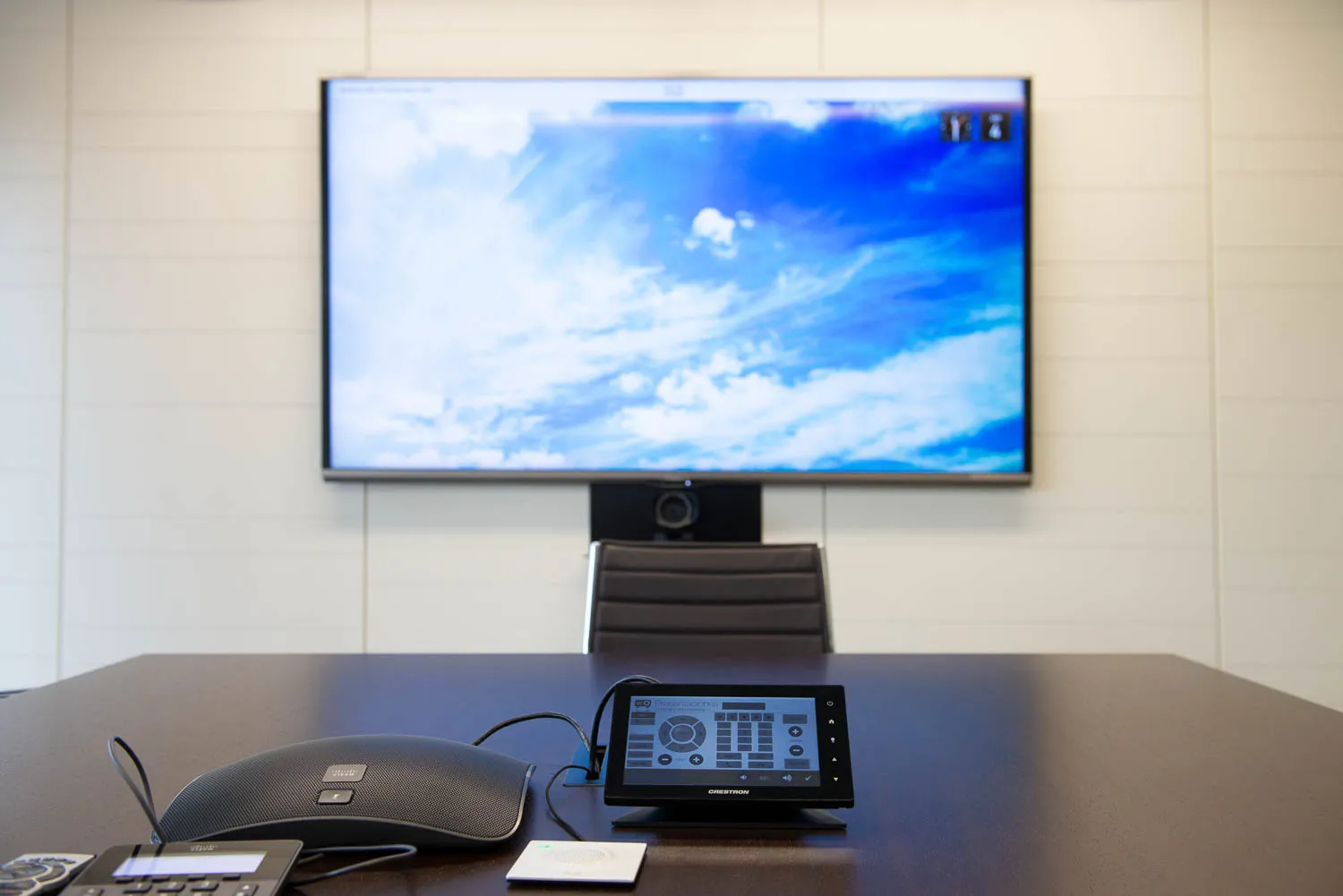 Sala de reuniones con pantalla de gran formato, cámara de videoconferencia y panel de control sobre la mesa.